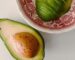 Close-up of a ripe, sliced avocado in a decorative red bowl on a white surface.