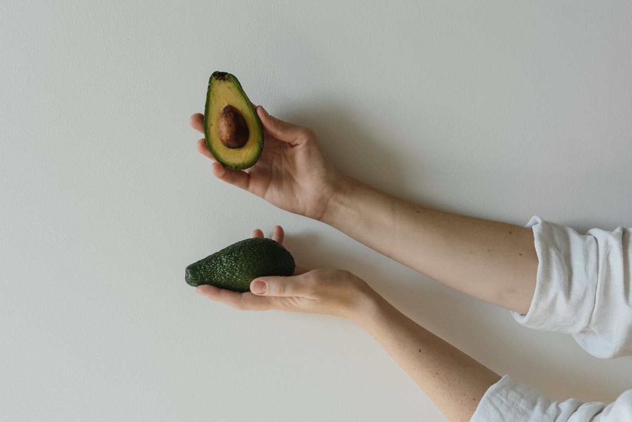 Minimalist image showing hands holding a whole and a sliced avocado, highlighting healthy food.